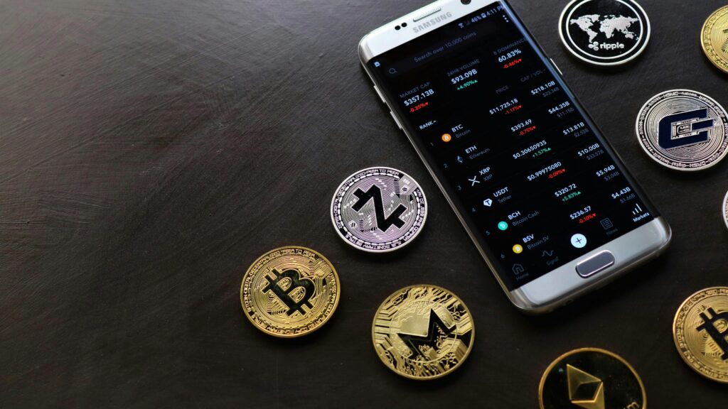 A collection of cryptocurrency coins and a smartphone displaying a digital trading platform.